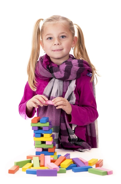 Loisirs des enfants, créativité, une petite fille vêtue d'une robe bleue jouant avec le jeu de bois jenga sur fond blanc