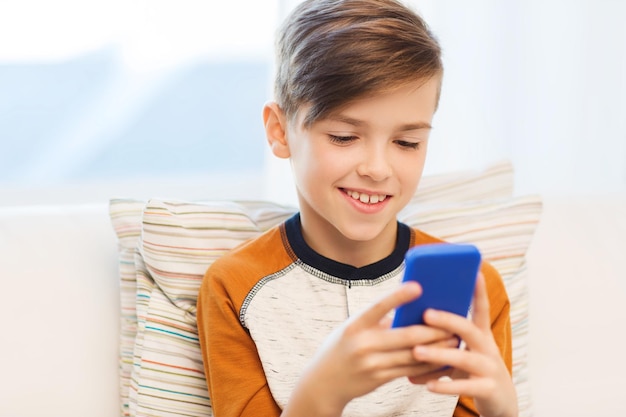 Loisirs, enfants, technologie, communication Internet et concept de personnes - garçon souriant avec un message textuel sur smartphone ou jouant à un jeu à la maison