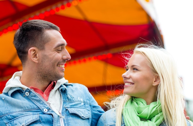 loisirs, parc d'attractions et concept d'amitié - couple souriant dans un parc d'attractions avec carrousel à l'arrière