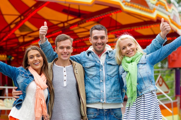 loisirs, parc d'attractions et concept d'amitié - groupe d'amis souriants montrant les pouces vers le haut avec un carrousel à l'arrière