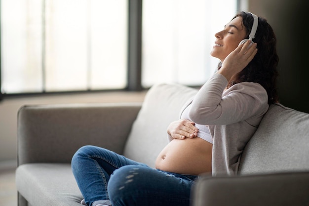 Loisirs pendant la grossesse femme enceinte heureuse écoutant de la musique dans des écouteurs à la maison