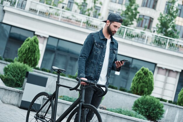 Loisirs de plein air jeune homme élégant marchant dans la rue de la ville avec un vélo sur Internet sur