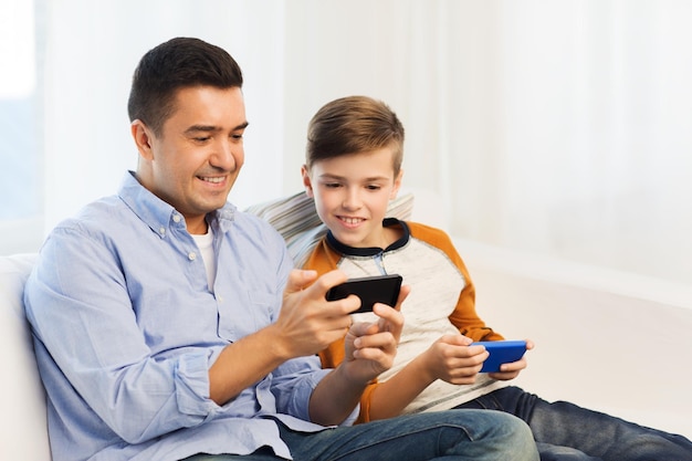loisirs, technologie, technologie, concept de famille et de personnes - père et fils heureux avec des smartphones envoyant un message textuel ou jouant à un jeu à la maison
