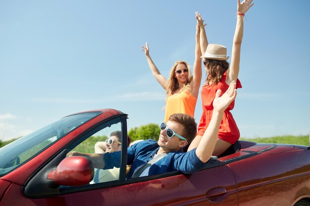 loisirs, voyage sur la route, voyage et concept de personnes - amis heureux conduisant en voiture cabriolet au pays et agitant les mains