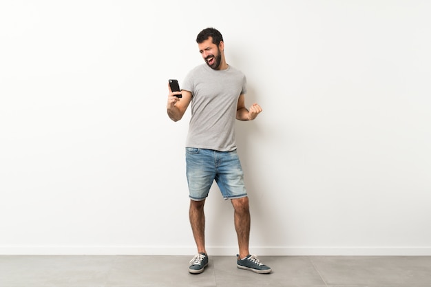 Un long coup de bel homme avec une barbe avec un téléphone en position de victoire