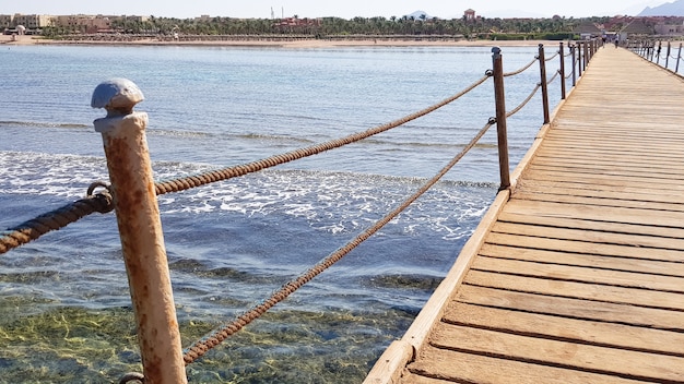 Long ponton sur la mer Rouge en Egypte. Ponton pour la descente dans l'eau. Pont en bois sur le territoire de l'hôtel Amway à Sharm El Sheikh avec des clôtures métalliques et une corde au-dessus de la mer avec des vagues.