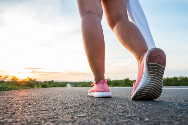 Le long de la route dans les collines au moment du coucher du soleil, la femme fait de l'exercice en courant.