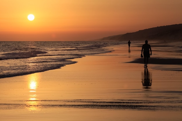 long shot de coucher de soleil incroyable sur l'océan avec la silhouette d'un homme qui marche