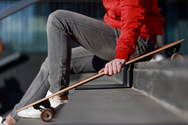 Longboarder homme en vêtements décontractés reposant sur les marches, assis avec longboard / skateboard à l'extérieur