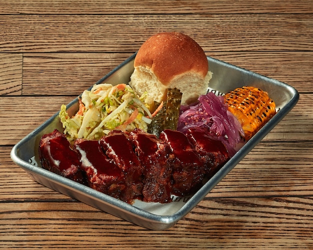 Longe de porc au four avec sauce barbecue et garniture de légumes sur un plateau en plastique