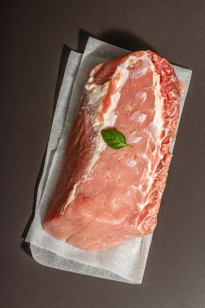 Longe de porc crue avec feuille de basilic. Gros morceau de viande, fond de béton de pierre noire. Lumière dure à la mode, ombre sombre, vue de dessus