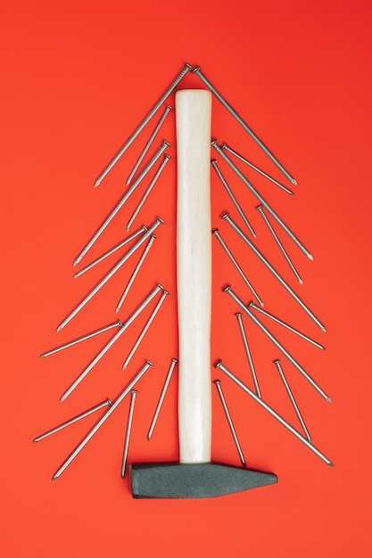 Photo longs clous et marteau, disposés en forme d'arbre de noël sur fond rouge. verticale. mise à plat