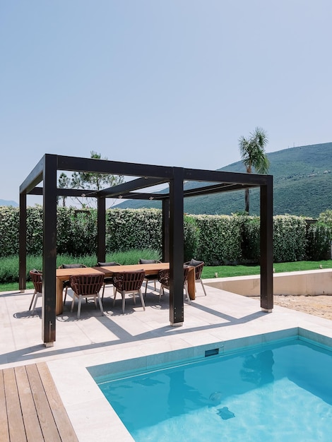 Longue table avec des chaises dans une pergola en bois près de la piscine