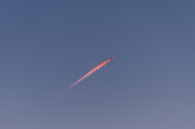 Une longue traînée de coucher de soleil rouge rose d'avion à réaction sur le ciel bleu.