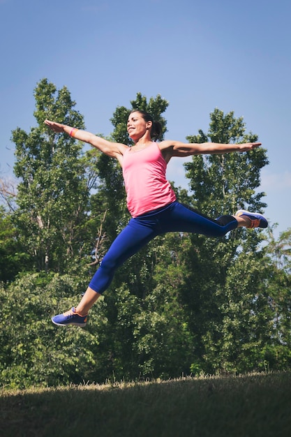 Longueur complète d'une femme avec les bras étendus sautant contre les arbres dans le parc