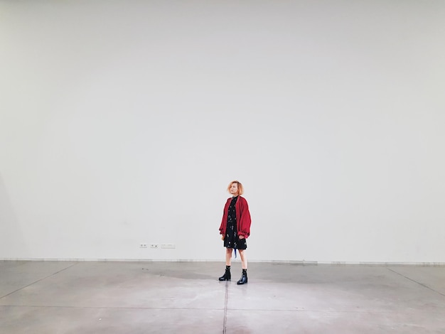 Photo la longueur complète de la femme détournant le regard alors qu'elle se tient contre le mur blanc