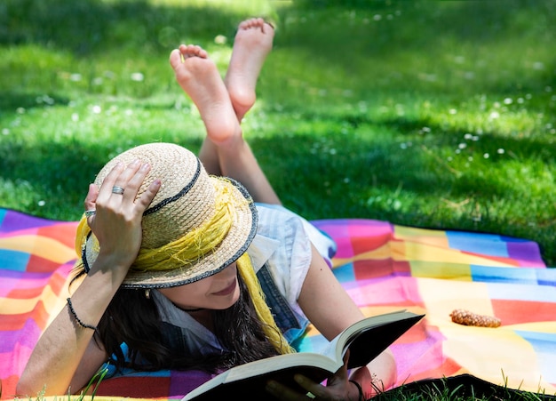 Photo la longueur complète d'une femme lisant un livre tout en se relaxant sur une couverture de pique-nique dans le champ