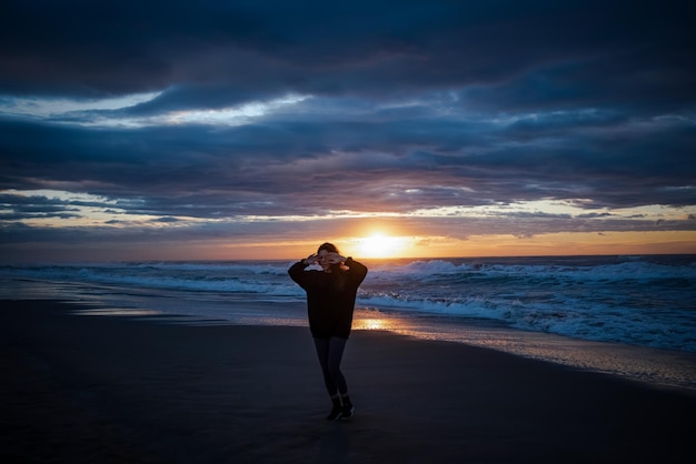 Longueur complète d'une femme marchant sur la plage au coucher du soleil