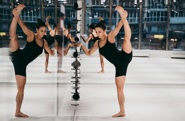 La longueur complète de la femme s'étirant en se tenant devant le miroir au gymnase