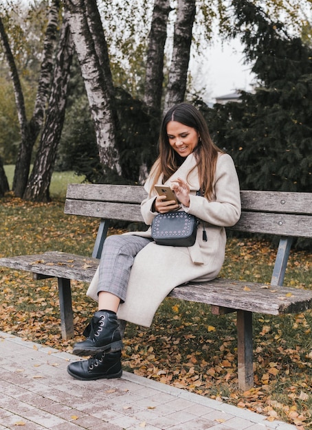 Photo la longueur complète de la femme utilisant le téléphone alors qu'elle est assise sur un banc dans le parc