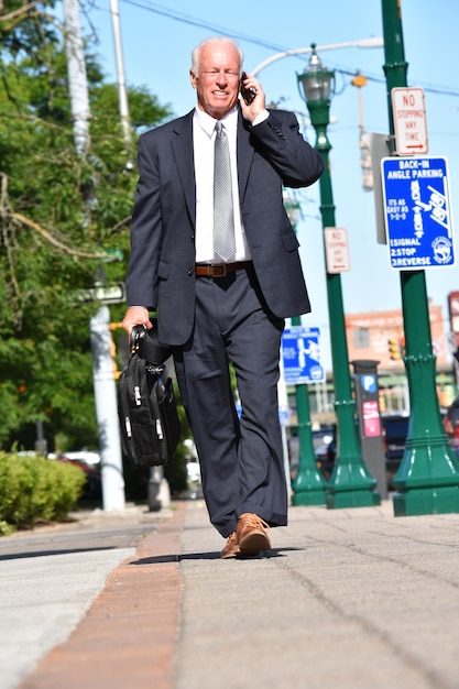 Photo longueur complète de l'homme d'affaires parlant au téléphone portable tout en marchant avec le sac sur la route
