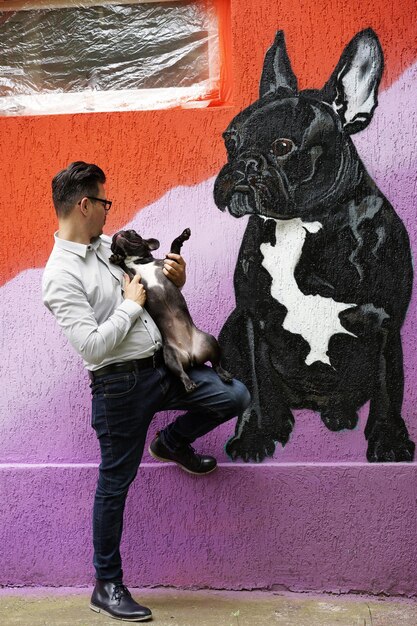 Photo longueur complète de l'homme avec le chien debout près du mur peint