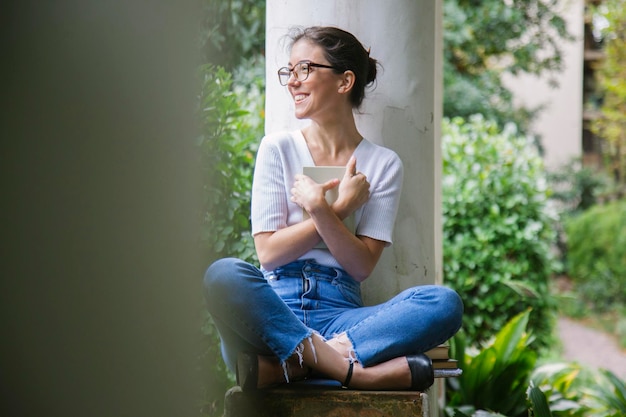 La longueur complète d'une jeune femme utilisant le téléphone alors qu'elle est assise à l'extérieur