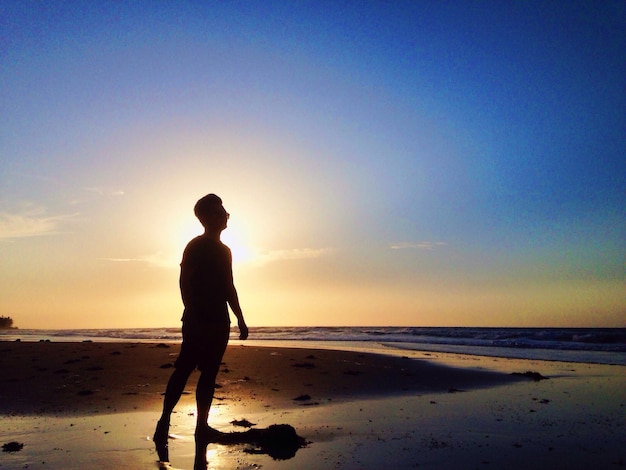 Longueur complète de la silhouette de l'homme debout sur la plage contre le ciel au coucher du soleil