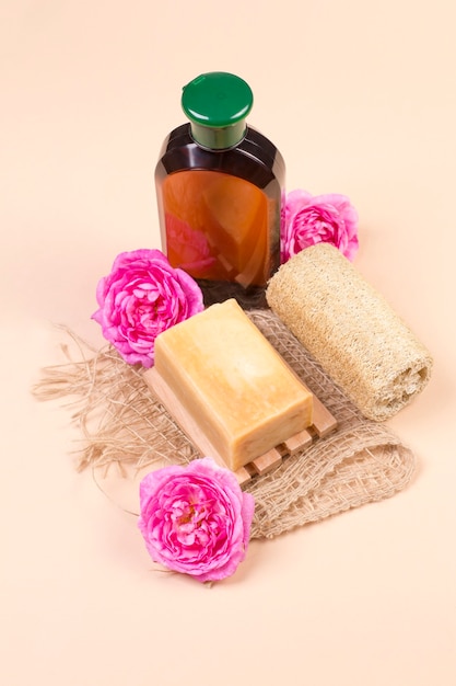 Loofah de savon naturel et une bouteille de produit cosmétique sur un fond beige avec des roses