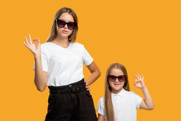 Look de famille Mode d'été Parentalité réussie Élégante mère confiante cool et petite fille dans des lunettes de soleil montrant le signe OK isolé sur fond d'espace de copie orange