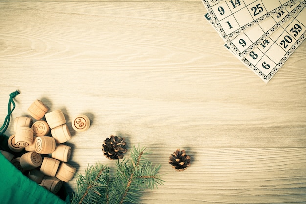 Loto de jeu de société. Barils de loto en bois avec sac et cartes de jeu, branches de sapin de Noël et cônes sur planches de bois. Vue de dessus. Effet tonifiant des couleurs.