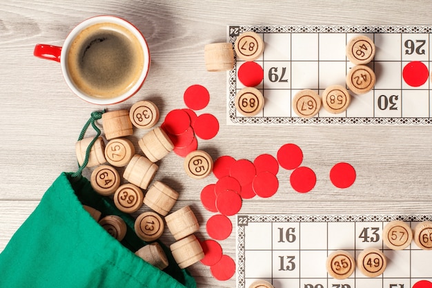 Loto de jeu de société. Barils de loto en bois avec sac vert, cartes de jeu, jetons rouges et tasse de café. Vue de dessus