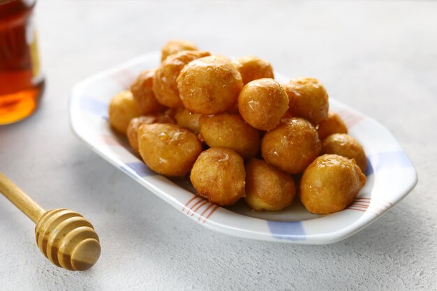 Loukoumades luqaimat ou lokma avec sauce au miel dans une assiette à fond blanc