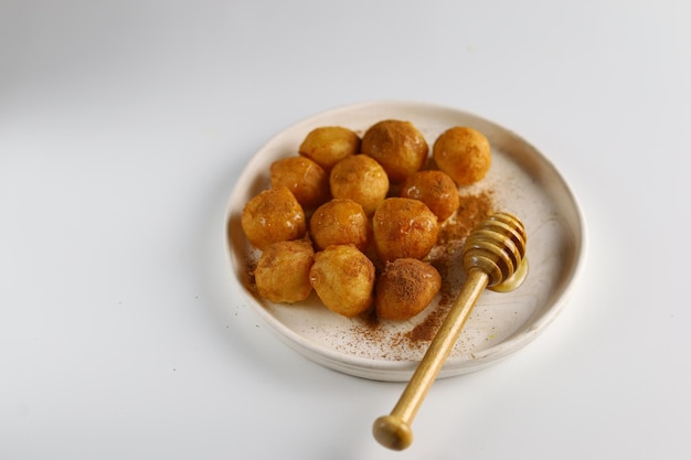 Loukoumades luqaimat ou lokma avec sauce au miel dans une assiette à fond blanc