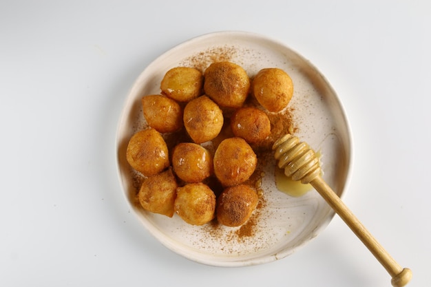 Loukoumades luqaimat ou lokma avec sauce au miel dans une assiette à fond blanc