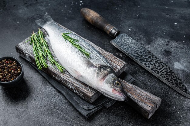 Loup de mer cru frais ou poisson de bar sur une planche de bois prêt pour la cuisson. Fond noir. Vue de dessus.