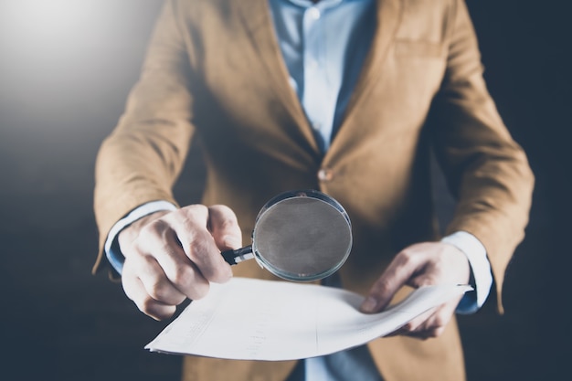 Loupe de main de l'homme avec document sur fond sombre