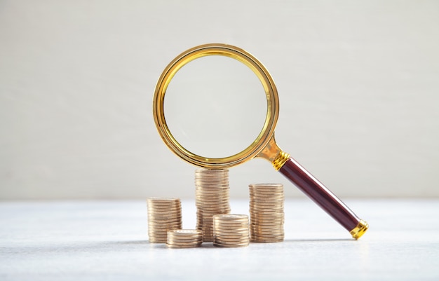 Loupe et pièces de monnaie sur le bureau blanc.