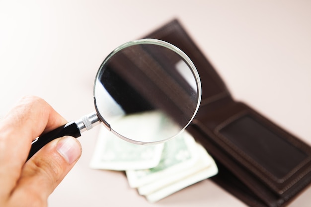 La loupe regarde le portefeuille avec de l'argent sur la table