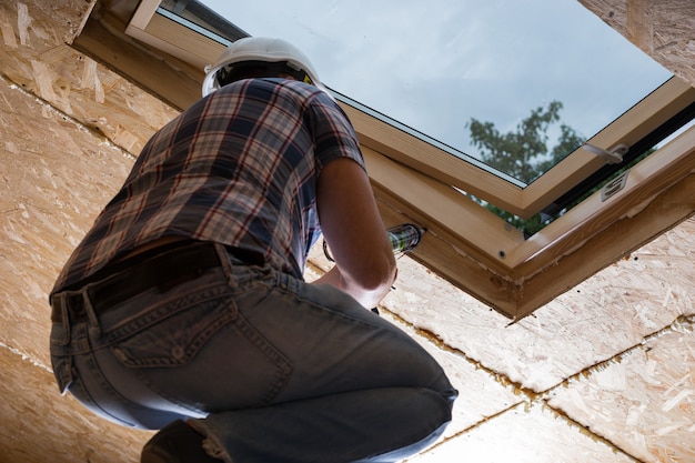 Low Angle View of Male Construction Worker Builder appliquant du calfeutrage frais à la lumière du ciel au plafond de la maison inachevée