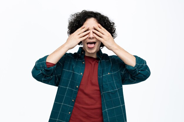 Ludique jeune bel homme fermant les yeux avec les mains et montrant la langue isolé sur fond blanc