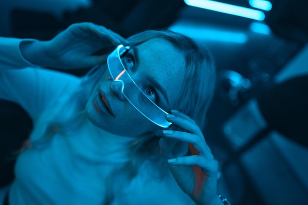 La lumière bleue au néon tombe sur une jeune femme portant des lunettes de verre futuristes photo de haute qualité