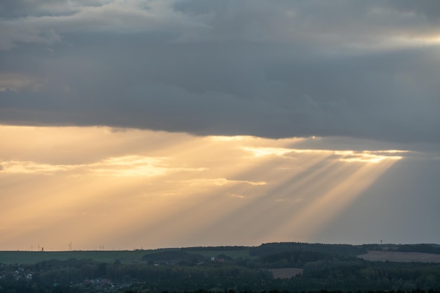 La lumière du soleil traverse les nuages en lignes droites et tombe sur la ville et la forêt Le soleil était caché derrière les nuages La forêt dans les rayons du soleil couchant