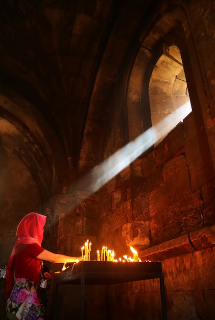 La lumière naturelle du soleil brille dans une église médiévale d'une femme allumant des bougies