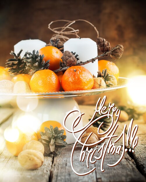Lumière de Noël sur la table de fête avec mandarines, pommes de pin, noix de Grenoble, bougies.