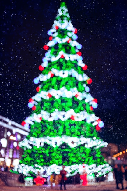 Lumières d'arbre de Noël défocalisées colorées sur fond de ville et neige la nuit