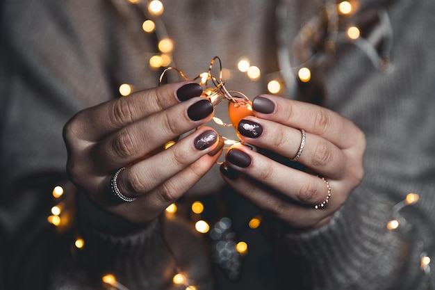 Lumières dans les paumes. Mains de femmes tenant une guirlande. Fille dans un pull bleu avec des lumières de Noël dans ses mains, ambiance chaleureuse de Noël, mise au point douce