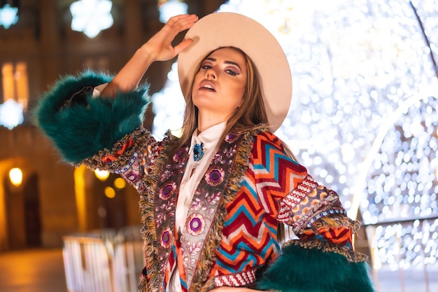 Lumières de Noël dans la ville, modèle blonde avec un chapeau à côté d'une boule lumineuse géante dans une pose à la mode, mode de vie hivernal