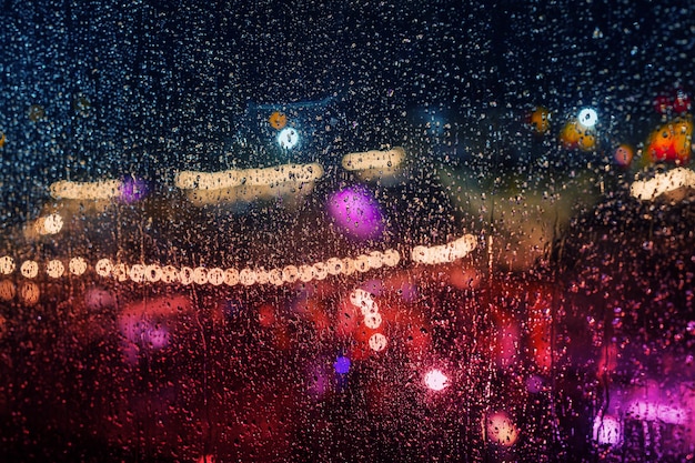 Lumières de la ville de la nuit pendant la pluie derrière un verre recouvert de gouttes d'eau.