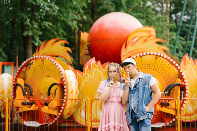 Lumineux couple gai amoureux se reposant dans un parc d'attractions. Funny guy et fille mangeant des sucettes sur un bâton